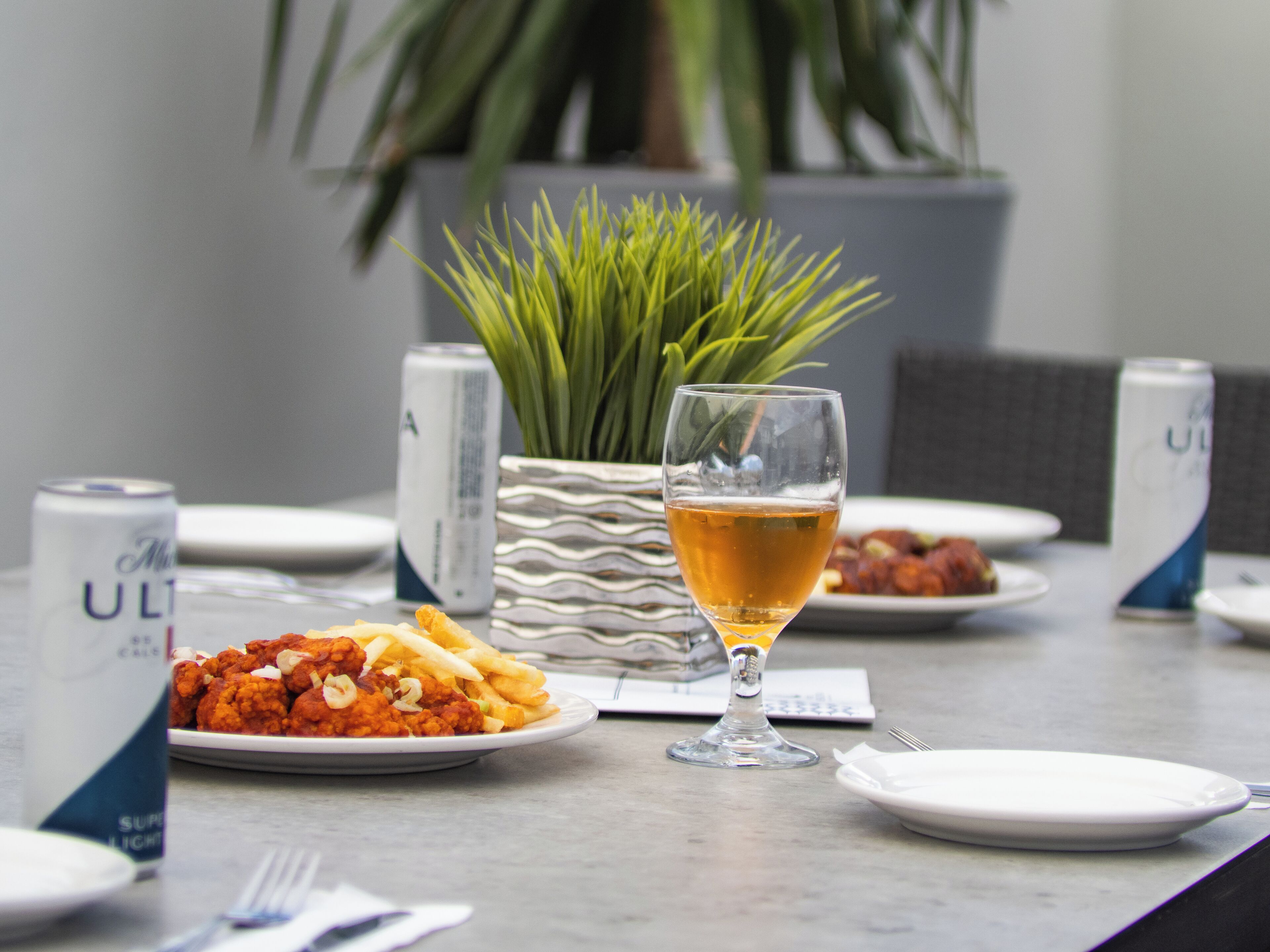 A dining table with plates of food, a glass of beer, and cans of beer.