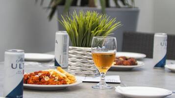 A dining table with plates of food, a glass of beer, and cans of beer.