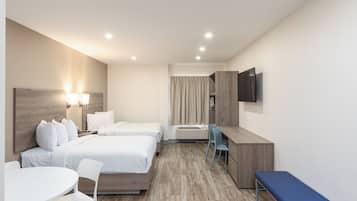 Quarto de hotel com duas camas, uma escrivaninha, uma cadeira, um banco, uma televisão e uma janela com cortinas.