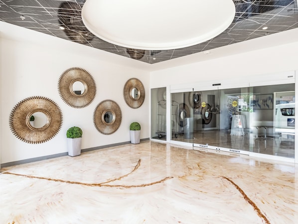 Un vestíbulo moderno con piso de mármol, espejos en la pared y plantas en macetas.