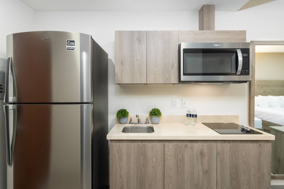 A modern kitchen with a stainless steel refrigerator, a microwave, a sink, and wooden cabinetry.