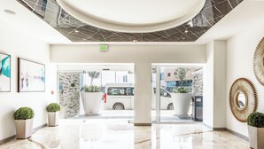 Un hall d’entrée moderne avec un sol en marbre, une grande plante en pot et une porte vitrée donnant sur l’extérieur.