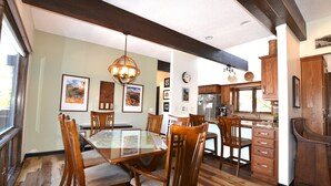 A dining area with a glass-top table surrounded by wooden chairs, a wooden ceiling, and a kitchen with wooden cabinets and a refrigerator. - Dreamcatcher - 2 bed 2 bath condo with tremdous views! (Estes Park)