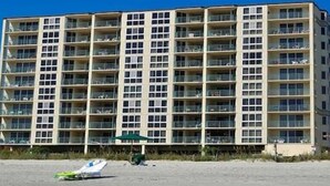 Ein mehrstöckiges Hotel mit einheitlichem Äußeren und Balkonen auf jeder Etage, vor dem sich ein Strand erstreckt.