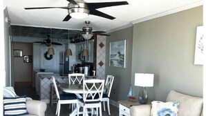 Ein modernes Wohnzimmer mit Essbereich, Deckenventilator und einer Küche im Hintergrund.