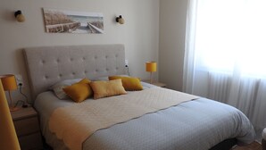 Un letto rifatto con cura, un quilt grigio e due cuscini color senape, un quadro appeso alla parete e due abat-jour.