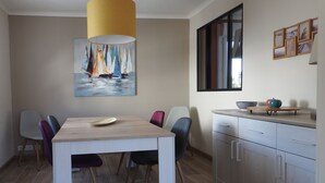Zona pranzo con tavolo e sedie in legno, una lampada a sospensione gialla e un quadro con velieri sulla parete.