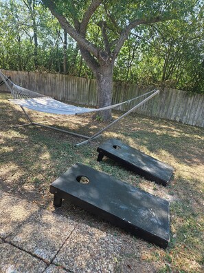 A hammock tied between two trees in a backyard with a wooden fence in the background.