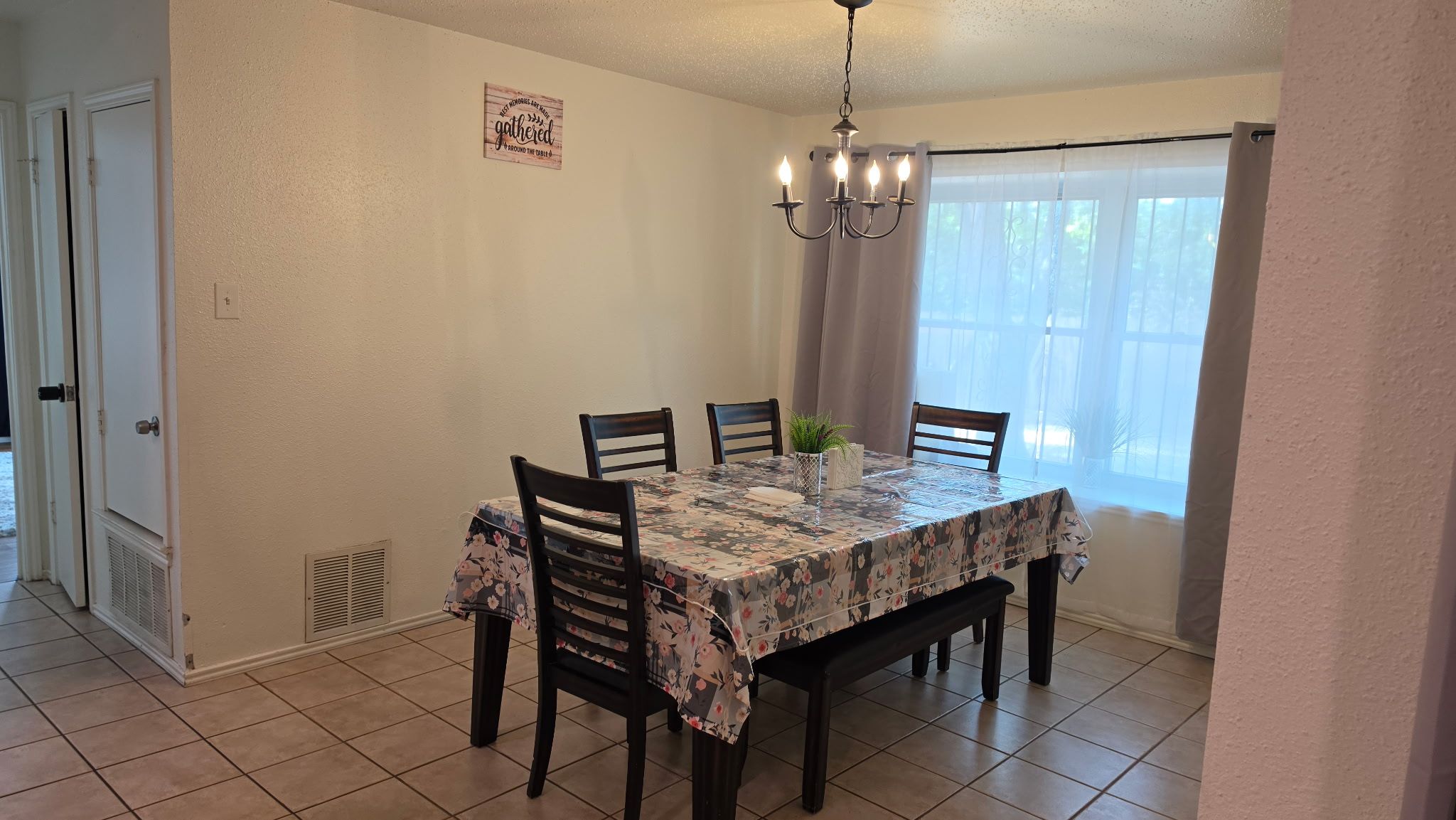 A dining area with a table set for four, a chandelier, and a window with curtains.