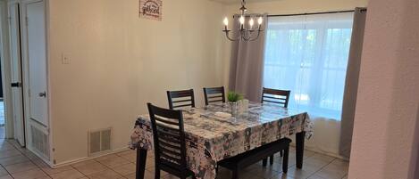 A dining area with a table set for four, a chandelier, and a window with curtains.