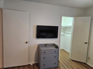 A room with a closed door, a dresser with drawers, a mounted television, and a closet with a door.