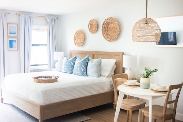 A neatly arranged bedroom with a large bed, bedside tables, a small table with chairs, and decorative woven items on the wall.