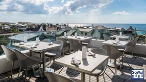 En tagterrasse med borde og stole, med udsigt over en kystby og havet.