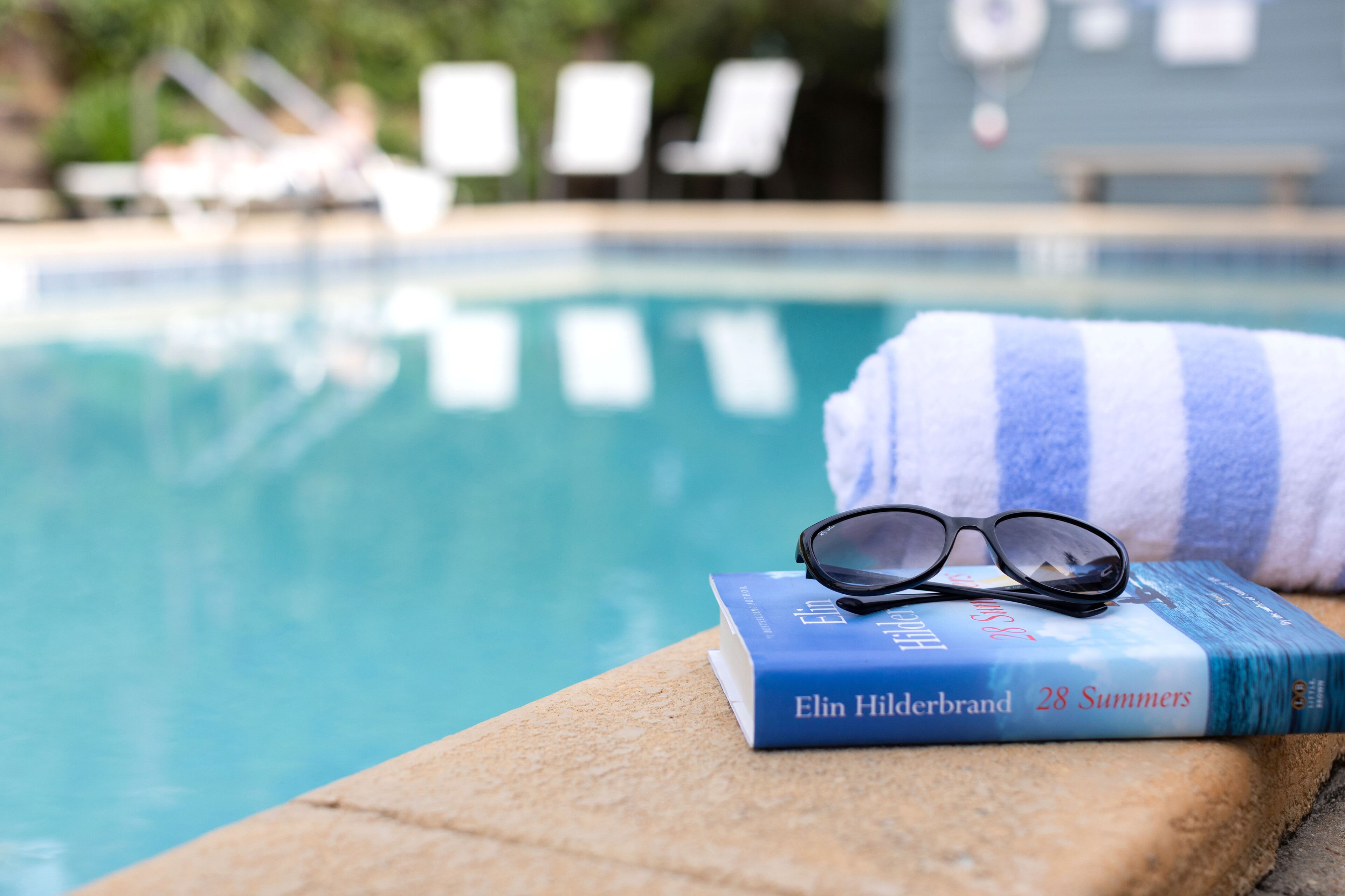 Un libro titulado '28 Summers' de Elin Hilderbrand sobre un borde junto a la piscina.