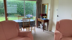 Una stanza con due poltrone rosa, un tavolo da pranzo con sedie, una scrivania con lampada e un'ampia finestra vista giardino.
