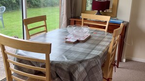 Zona pranzo con tavolo apparecchiato per quattro persone, una sedia di legno con cuscino a quadri e vista su un giardino verde attraverso un'ampia finestra.