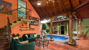 A spacious living area with a pool, green sofas, and a staircase leading to an upper level. - Casa Leona Colonial Home in Downtown Tamarindo (Tamarindo)