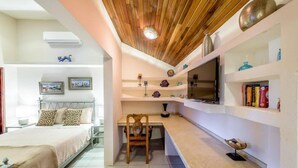 A bedroom with a bed, a desk, and a TV. There are shelves with decorative items and books. - Casa Leona Colonial Home in Downtown Tamarindo (Tamarindo)