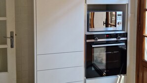 A kitchen with a built-in oven and microwave, a white cabinet, and a basket on top.