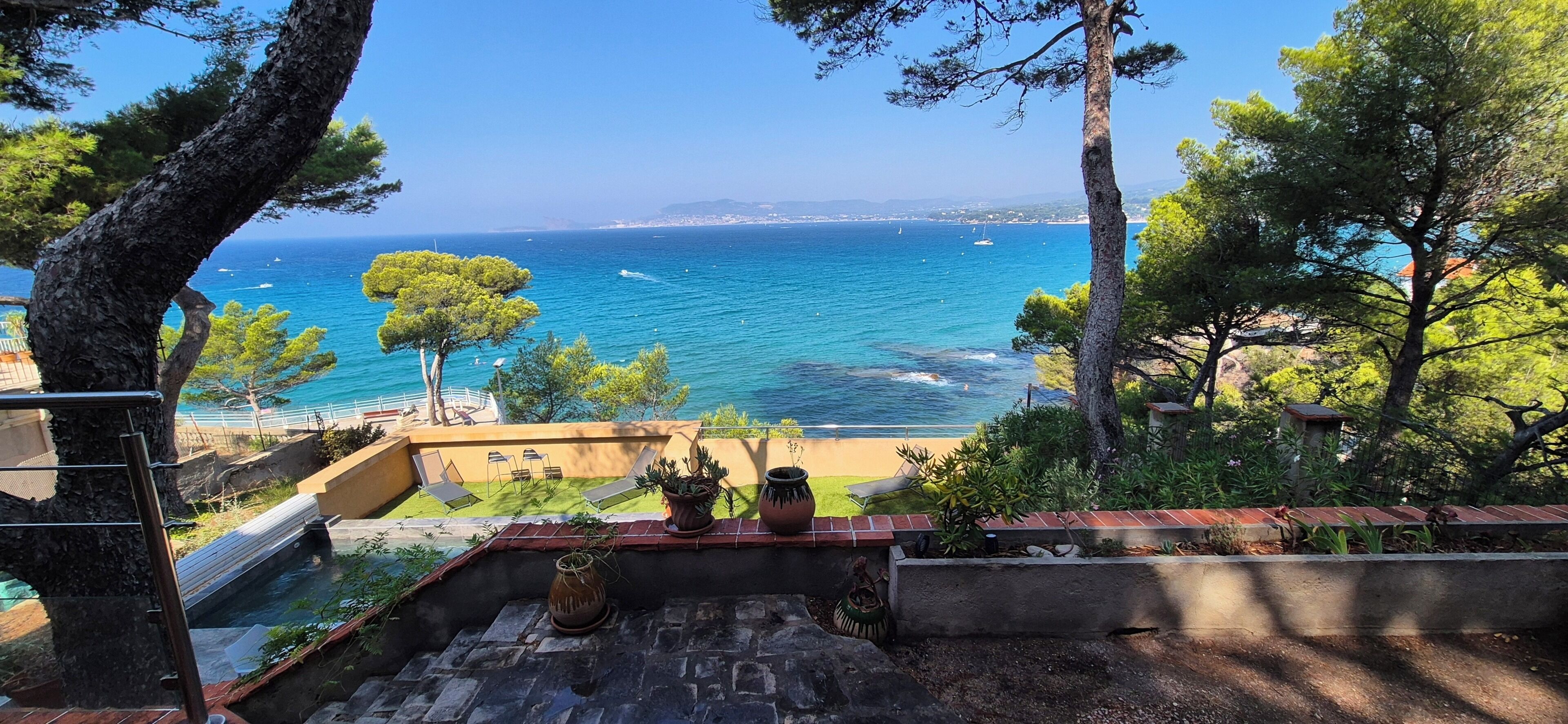 A terrace with a view of the sea, outdoor seating, and potted plants.