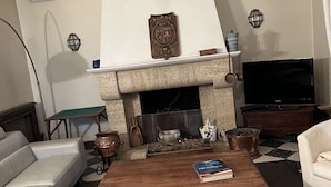 A living room with a fireplace, a sofa, a coffee table with books, and a television.