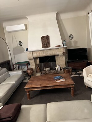 A living room with a fireplace, a sofa, a coffee table with books, and a television.