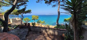 Vista costanera amb cel blau, un balcó amb plantes en testos i una paret de pedra.