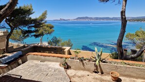 A terrace with a view of the sea, outdoor seating, and potted plants.