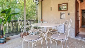 Une terrasse avec une table ronde et des chaises en métal blanc, entourée de plantes en pot.