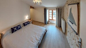 Une chambre à coucher avec un grand lit, une table de chevet, une lampe, une fenêtre avec des rideaux et un radiateur au mur.