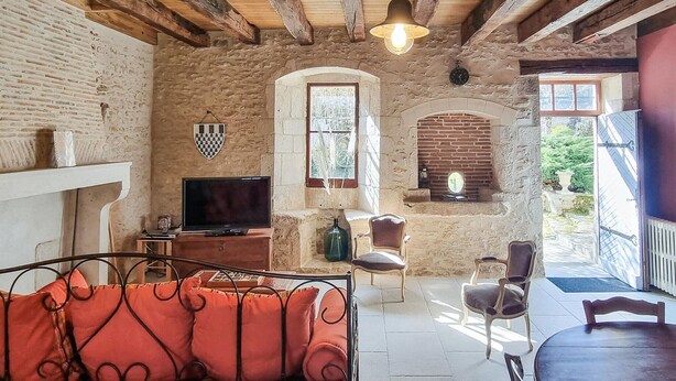 Une pièce rustique avec des murs en briques apparentes, une télévision, une cheminée et un coin repas comprenant une table et des chaises.