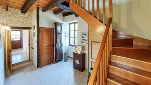 Un escalier en bois menant à un deuxième étage, une grande porte en bois, une horloge murale et une petite table sur laquelle est posé un objet décoratif.