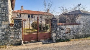 Un bâtiment en pierre avec un portail en métal, un toit recouvert de tuiles rouges et un ciel dégagé.