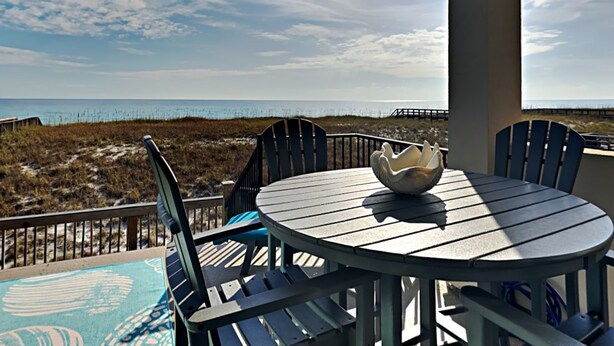 Een overdekt terras met een tafel en stoelen, met uitzicht op een strand en de oceaan.