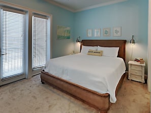 Un dormitorio con una cama grande, dos mesitas de noche y un ventanal con persianas.
