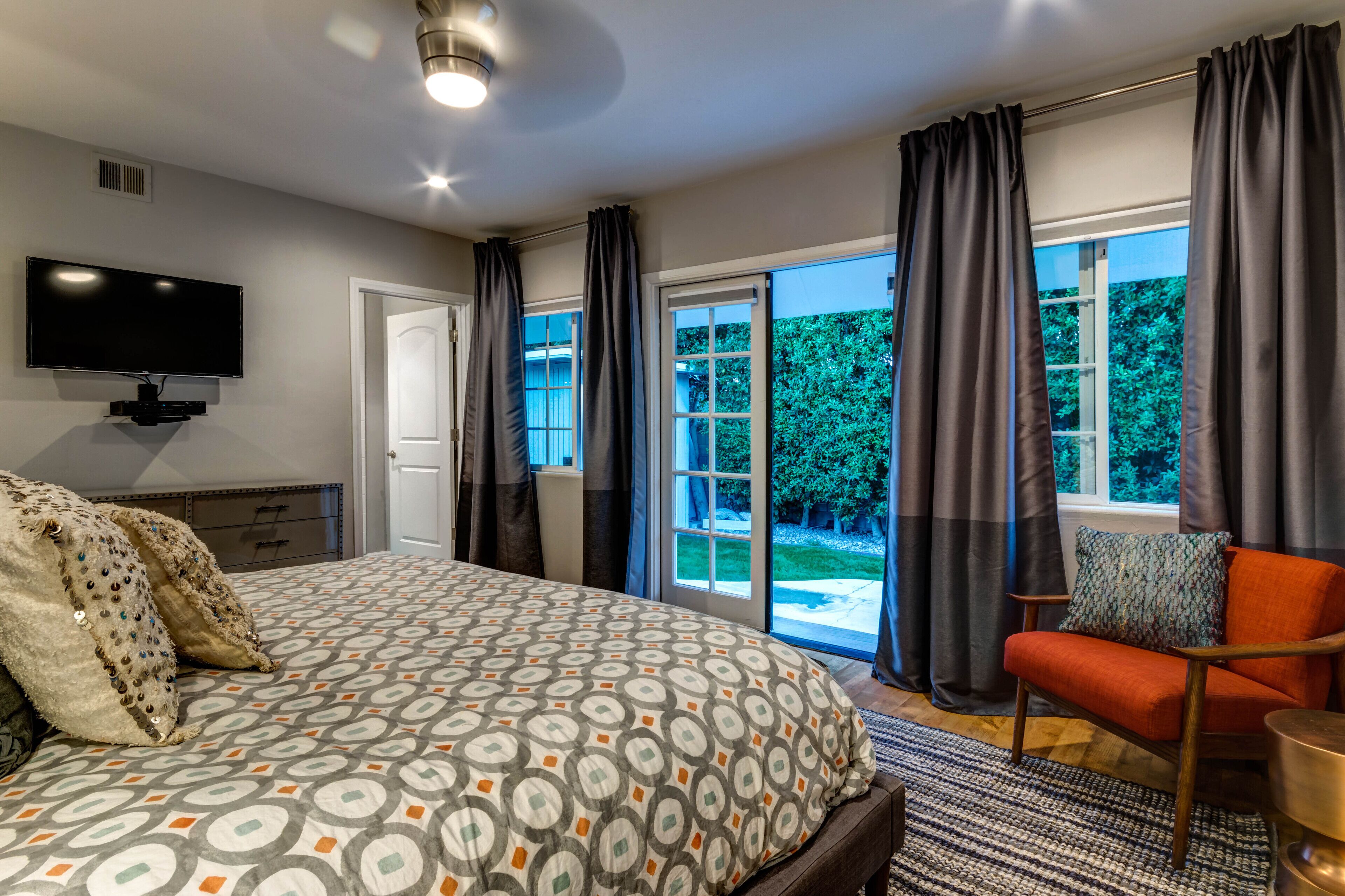 Ein Schlafzimmer mit einem Bett, einem Fernseher, einem Sessel und einer Glastür, die zu einem Garten führt.