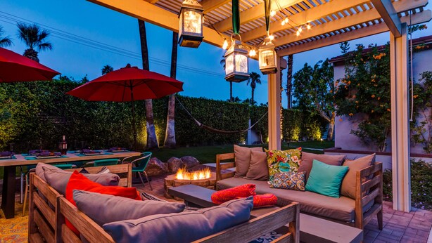 Un patio al aire libre con mobiliario de madera, sombrillas rojas y un hogar para fogata.
