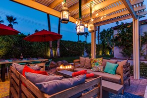 Eine Terrasse im Freien mit Holzmöbeln, roten Sonnenschirmen und einer Feuerstelle.