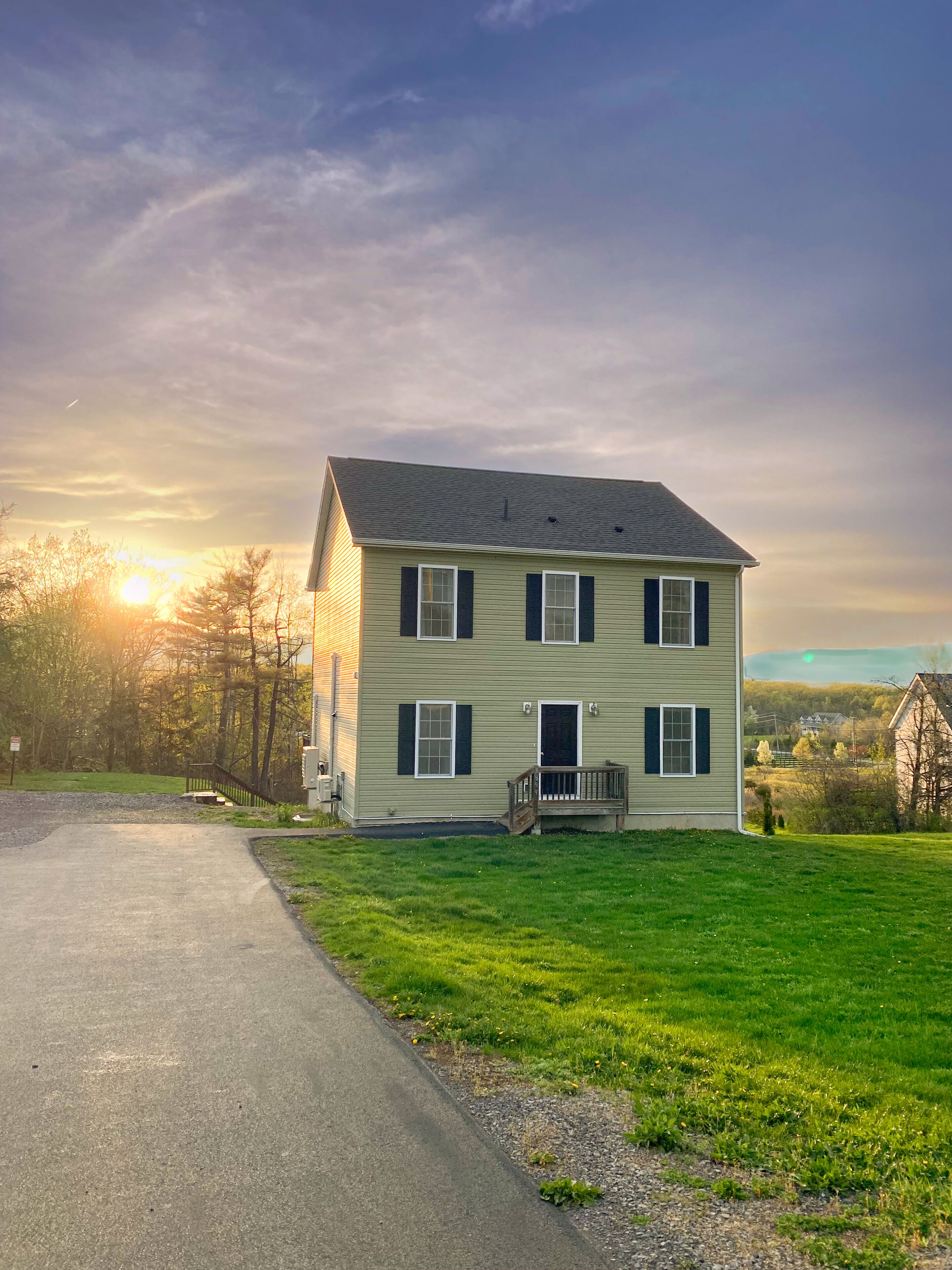 A two-story house with a front porch, a driveway, and a grassy yard.