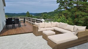 A covered outdoor seating area with a wicker sectional sofa and a table with chairs. - Great cabin in a central location (Agder)