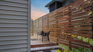 A wooden deck with two chairs and a table, surrounded by a wooden fence. - Walk to Beach, Full Kitchen, Cozy Surf Studio (Carolina Beach)