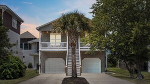 A two-story house with a front porch, a palm tree, and two garage doors. - Walk to Beach, Full Kitchen, Cozy Surf Studio (Carolina Beach)