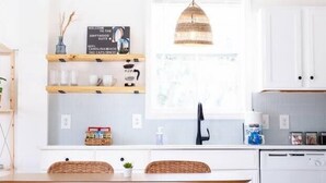 A modern kitchen with white cabinets, a wooden dining table with wicker chairs, a pendant light, and a ceiling fan. - Walk to Beach, Full Kitchen, Cozy Surf Studio (Carolina Beach)