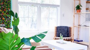 A bright living room with a white coffee table, a wooden chair, and a bookshelf. - Walk to Beach, Full Kitchen, Cozy Surf Studio (Carolina Beach)