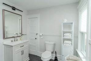 Un bagno moderno con un mobile vanità bianco, uno specchio grande, un WC e una finestra con persiane.