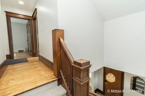 Una scala in legno con corrimano, gradini rivestiti di moquette e una porta in legno in cima.