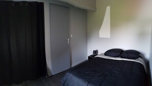 A bedroom with a bed, a nightstand, a lamp, and a door. - Petite Maison Moderne à la Campagne (Saint-Paulien)
