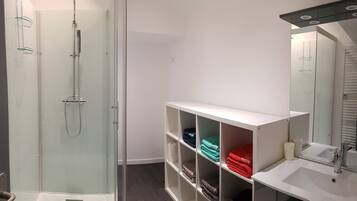 Een moderne badkamer met een douchecabine van glas, een witte wastafel met spiegel en keurig opgevouwen handdoeken.