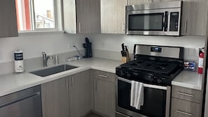 A modern kitchen with stainless steel appliances, a sink, and light wood cabinets. - Home Away From Home (Reno)