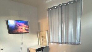 A bedroom with a bed, a TV mounted on the wall, a desk, and a window with curtains. - Home Away From Home (Reno)
